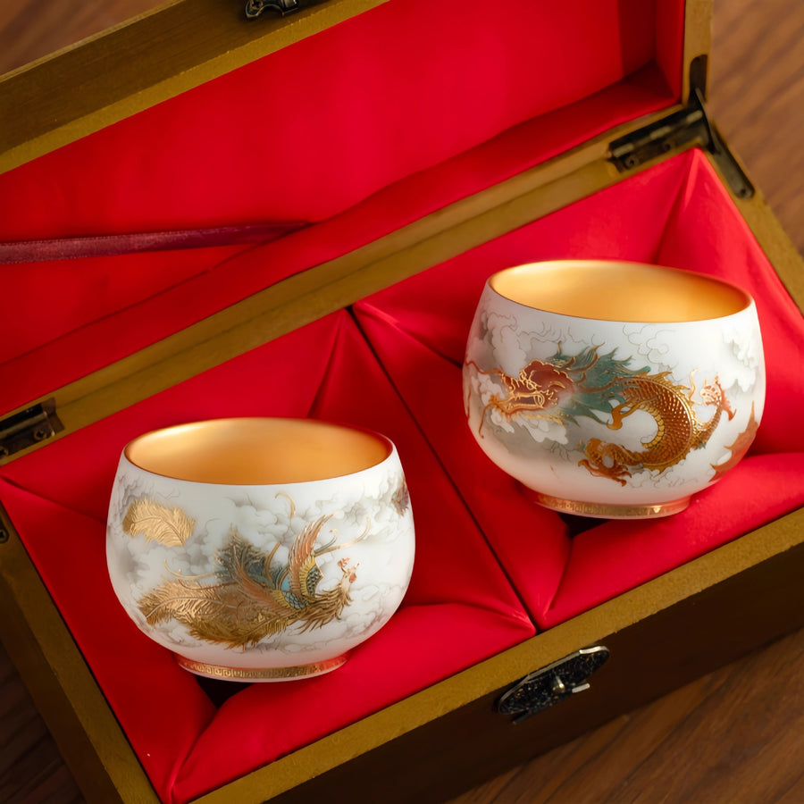 Two white ceramic teacups with dragon and phoenix designs in a red-lined wooden box