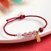 Close up of a red string bracelet with pink strawberry quartz beads and a gold tone lucky cat charm