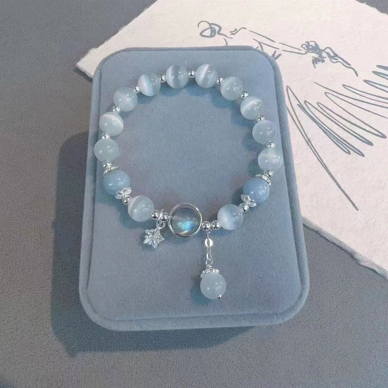 Blue glass cat's eye bracelet with silver star charm on a grey display stand