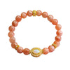 Peach moonstone beaded bracelet with a gold oval charm on a white background