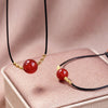Close up of a red agate bead necklace with gold-tone woven details on a black cord
