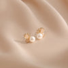 A pair of gold-tone butterfly stud earrings with freshwater pearls on soft fabric.