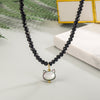 Close up of a white shell cat pendant hanging from a black beaded necklace