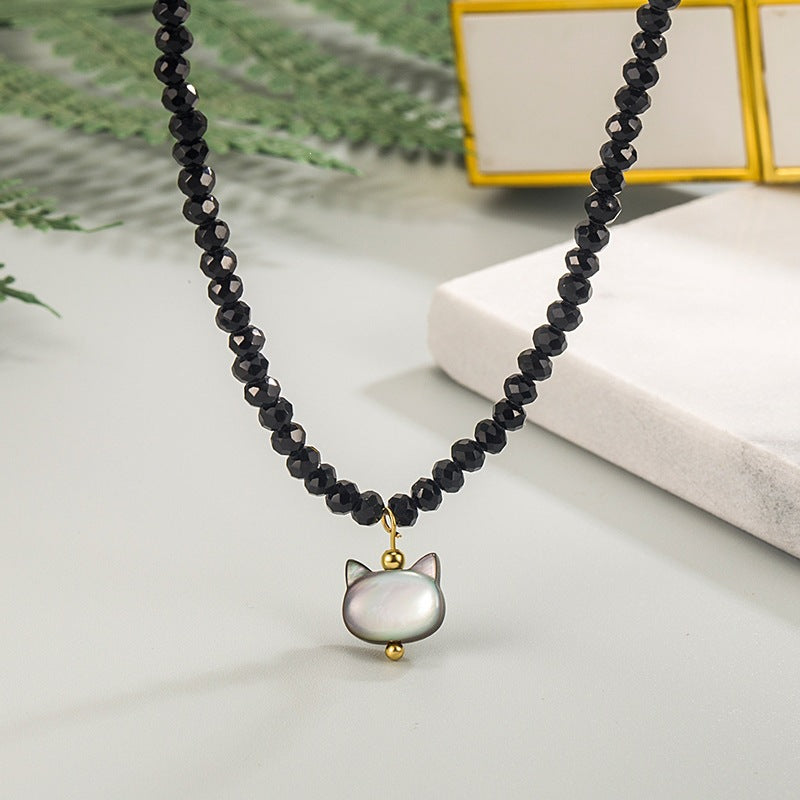 Close up of a white shell cat pendant hanging from a black beaded necklace
