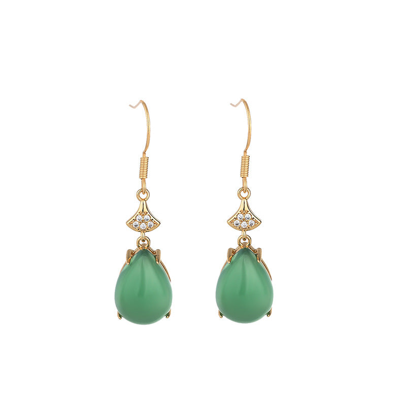 Pair of gold-tone hook earrings with green teardrop agate stones on a wooden surface