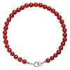 Close up of a thin red agate bead bracelet with a gold tone clasp on a white surface