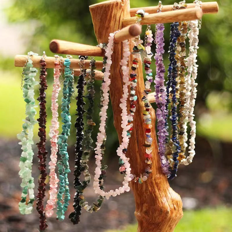 A row of colorful crushed stone chip necklaces hanging on a wooden display stand outdoors