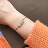 A woman's wrist wearing a thin yellow cord bracelet with three light green jade beads.