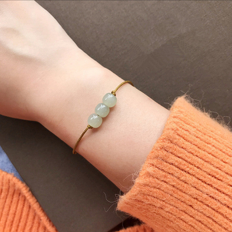 A woman's wrist wearing a thin yellow cord bracelet with three light green jade beads.