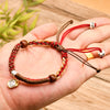 Hand holding a red and brown braided rope bracelet with a gold star charm