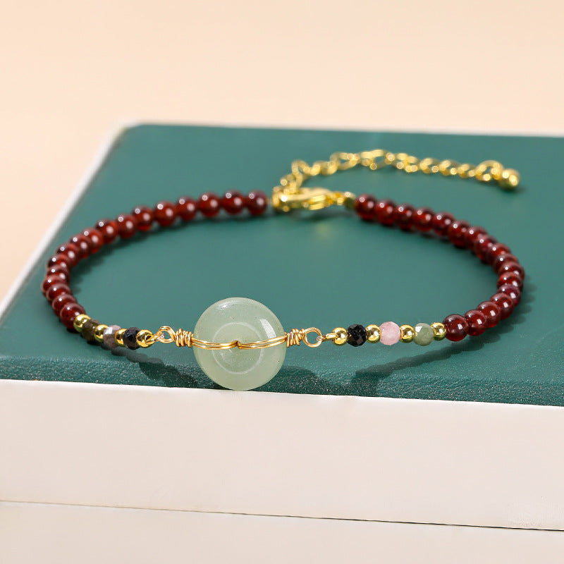 Close up of a red beaded bracelet with a light green peace buckle charm on a wrist