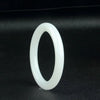 A slender, polished white jade bangle standing upright on a black surface