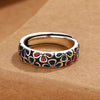 Close-up view of a copper ring with a colorful enamel plum blossom pattern on a brown background