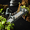 Miniature grey suspension bridge set among green plants and rocks