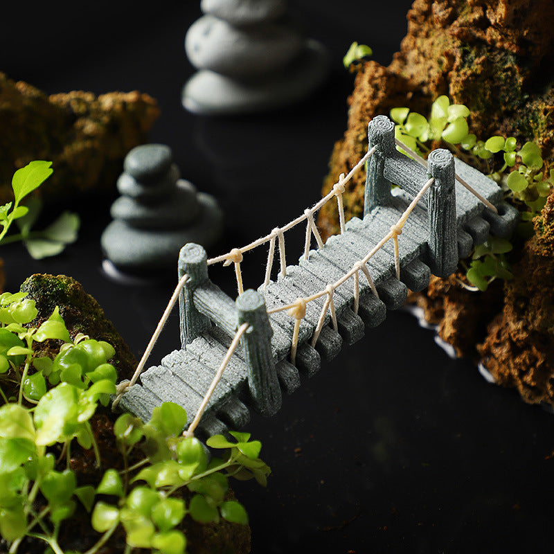 Miniature grey suspension bridge set among green plants and rocks