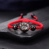 Close up of a silver sheen obsidian cat paw charm on a red braided bracelet