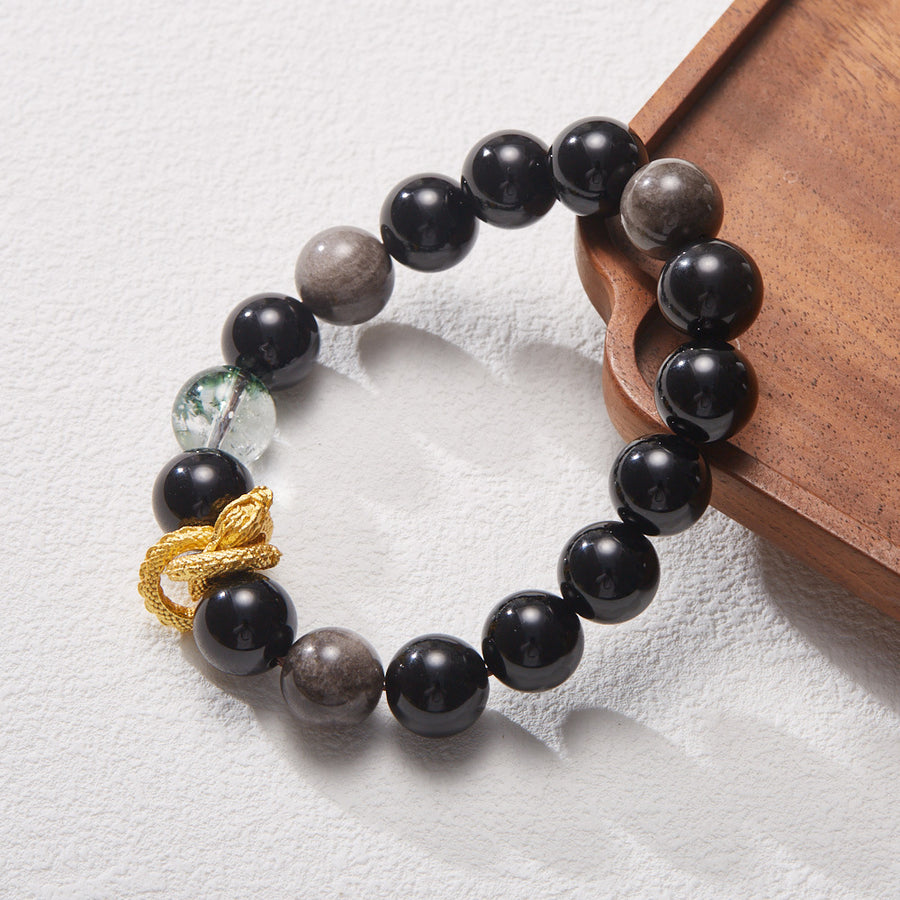 Close-up of a black obsidian bracelet with a gold dragon charm and a green phantom bead.