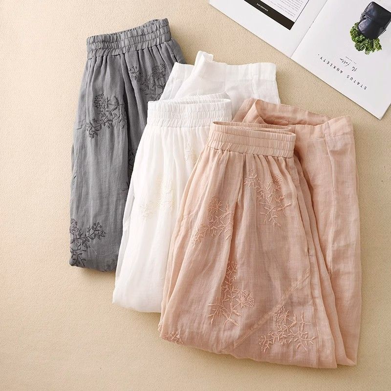 Three pairs of embroidered linen harem pants in grey white and pink laid flat