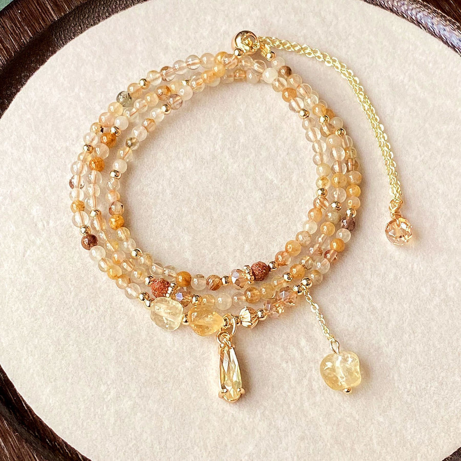 Close up of a multi strand yellow rutilated quartz bracelet with gold tone charms