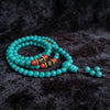 Coiled turquoise 108 bead mala bracelet with red accent beads on a dark background