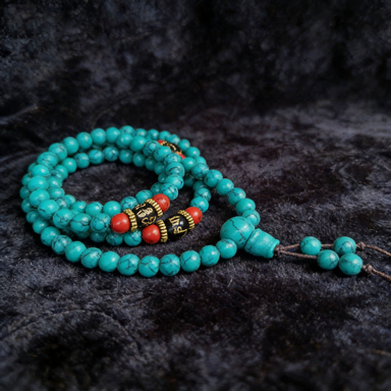 Coiled turquoise 108 bead mala bracelet with red accent beads on a dark background