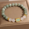 Close up of a beaded bracelet with green jade, white crystal beads and a gold mantra charm