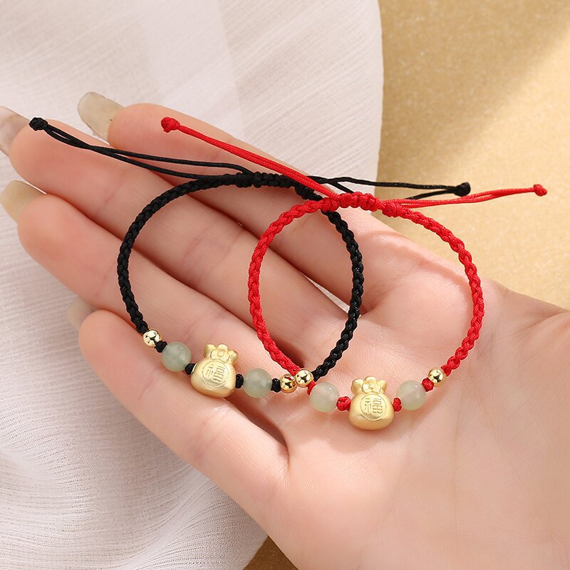 Gold-tone money bag charm on a braided cord bracelet held in hand