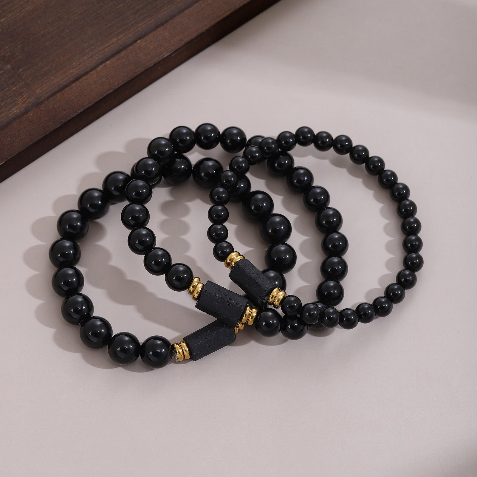 Three black bead bracelets with gold accents on a light surface