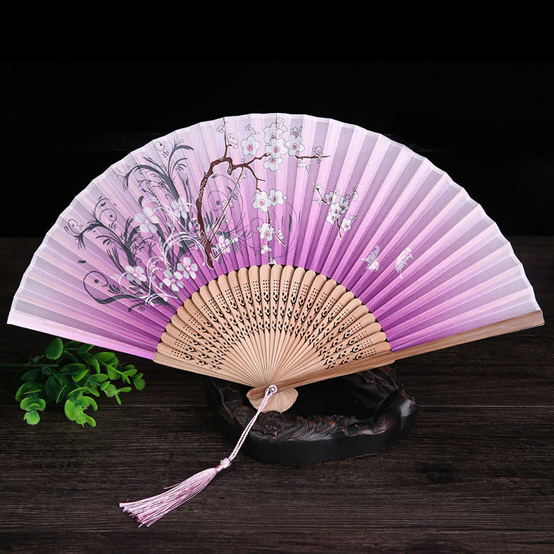 Open folding hand fan with purple gradient fabric and white flower painting on a wooden stand