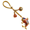 Close up of a brass koi fish keychain with a hollow bell and yellow cord held in hand