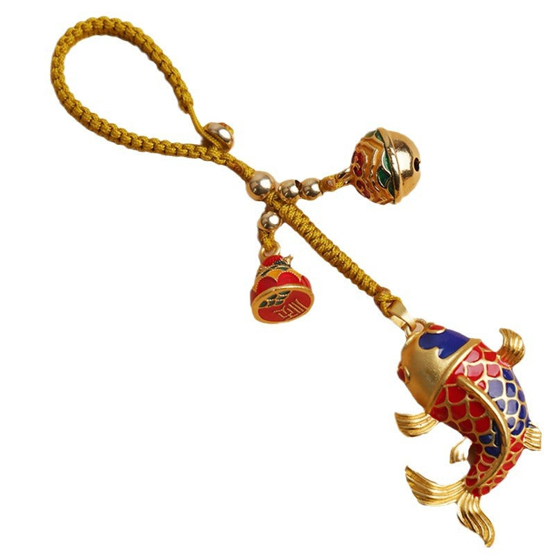 Close up of a brass koi fish keychain with a hollow bell and yellow cord held in hand