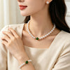 Woman wearing a white faux pearl necklace with a green stone accent and matching bracelet