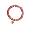 Close up of a pink strawberry quartz beaded bracelet with a gold lucky cat charm on a wrist