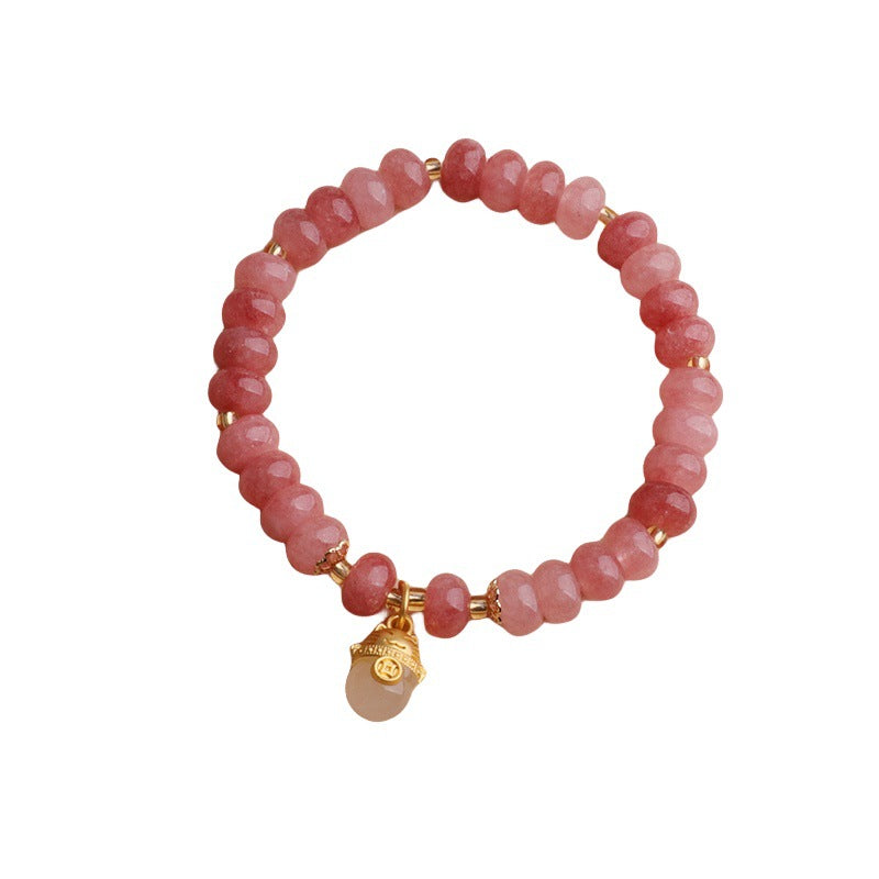Close up of a pink strawberry quartz beaded bracelet with a gold lucky cat charm on a wrist