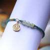Green braided bracelet with jade beads and a gold fortune charm on a wrist