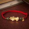 Close up of a red braided cord bracelet with a gold Pixiu charm and green beads