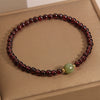 Close up of a thin red garnet beaded bracelet with one green jade bead on a box