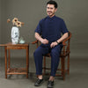 Man wearing a navy blue short sleeve tang suit set sitting on a wooden chair