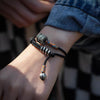 Close up of a wrist wearing a black wrap bracelet with a carved metal amulet.