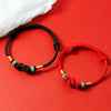 Red and black braided cord bracelets with a central knot and green glass beads on a red background