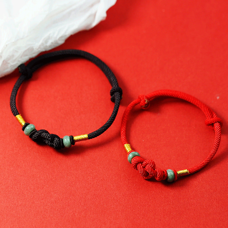 Red and black braided cord bracelets with a central knot and green glass beads on a red background