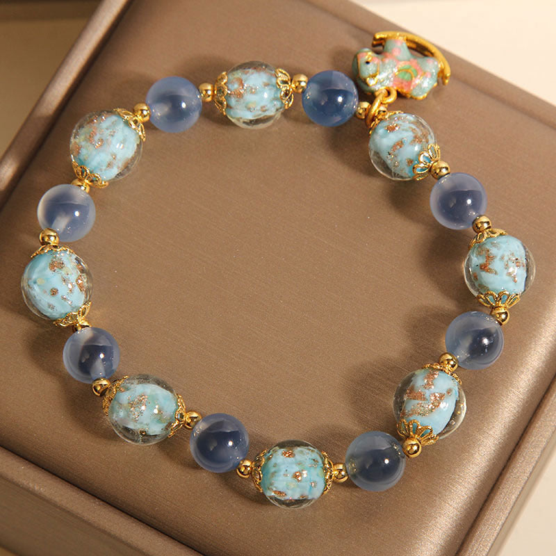 Blue beaded bracelet with gold spacers and a colorful rocking horse charm on a wooden surface