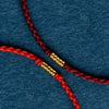 Close up of a braided red string bracelet with a gold tone bead on a blue background