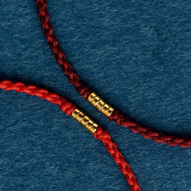Close up of a braided red string bracelet with a gold tone bead on a blue background