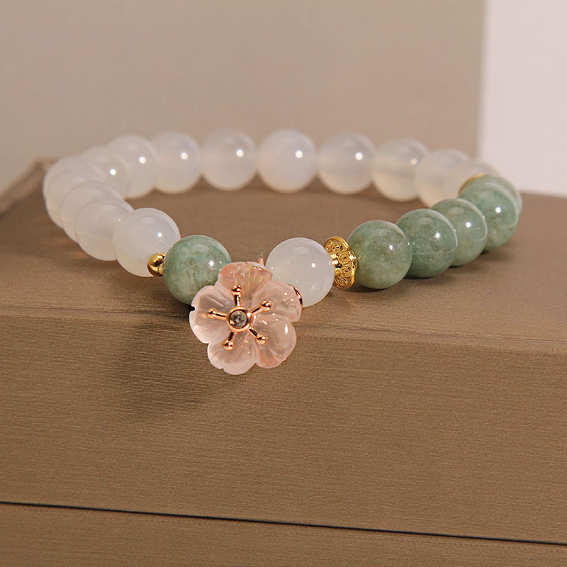 Close up of a white agate and jade beaded bracelet with a pink flower charm on a box