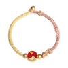 Close-up of a two-tone pink and yellow woven bracelet with gold-tone beads and a red mountain and sea charm.