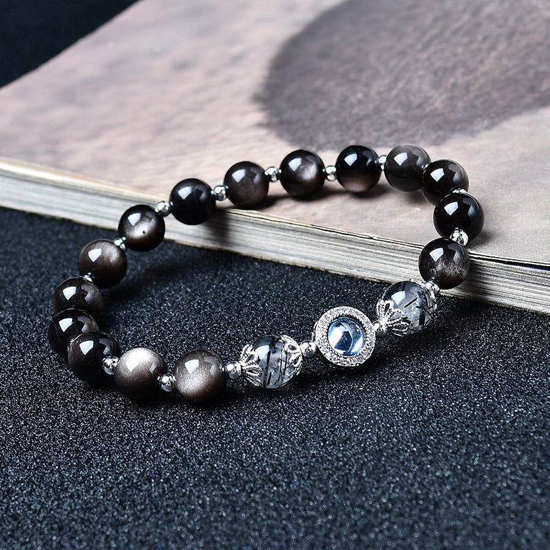 Black obsidian beaded bracelet with a blue stone centerpiece resting on an open book