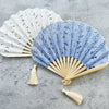 Open folding fan with white cotton fabric and hollow flower embroidery next to a blue one