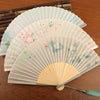 Three open folding fans with floral paintings and bamboo frames resting on a wooden surface