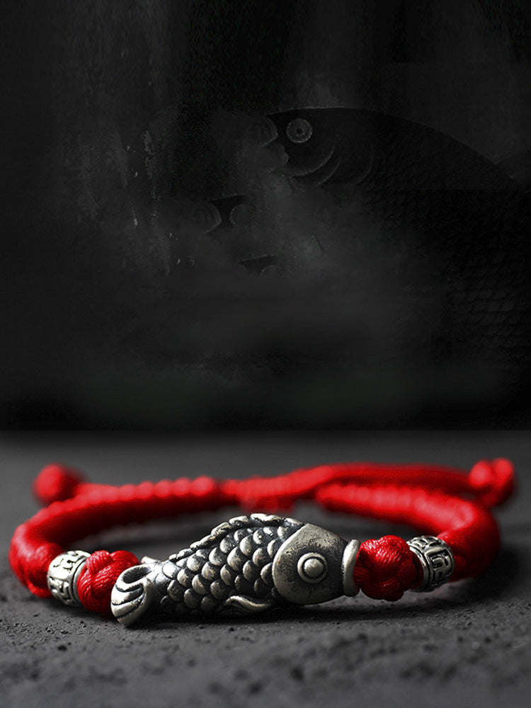 Close up view of a silver koi fish charm on a red braided bracelet